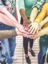 Hands from a group of seven teenagers meet in the middle of the photo.