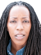 Image captures a headshot of Dr. Bettina L. Love. The phoot captures the NYU Metro Center 2026 Keyunote Speakers against a white backgroun with shoulder length locks. Dr. Love whears a blue collareded denim shirt with a red sportcoat.