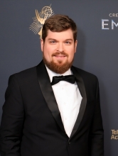 Alumni with beard standing in front of an Emmy banner