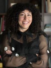 Christina is smiling in the center of the frame and has her arms crossed.