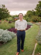 The photo shows a professional photo of Christian Wong in a garden posing for a photo in a white button down shirt and navy blue pants 
