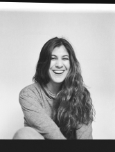 Black and white photo, Juliana is wearing a long sleeve shirt and is sitting center of frame smiling widely.