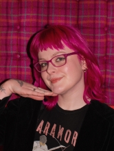 Student with raspberry colored hair posting in front of raspberry checked backdrop