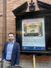 Paul Frucht stands in front of a Carnegie Hall poster