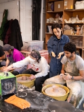 Students sit at wheels while the instructor looks over their work