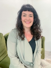 A white woman with dark hair smiles from a green couch.