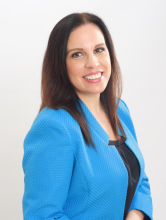 A woman with brown hair and a blue blazer smiles into the camera.