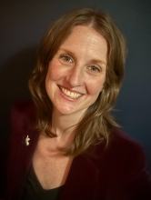 A white woman with light brown hair smiles in front of a blue backdrop.