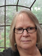 A white woman with short grey hair poses in front of a window.