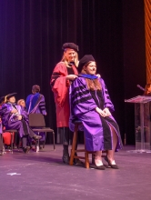 Patten drapes a hood over a doctoral graduate
