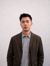 A young East Asian man with short black hair looks into the camera