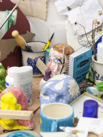 A snapshot of a ceramicist's studio. Paintbrushes and glue and ceramics all over a table. 