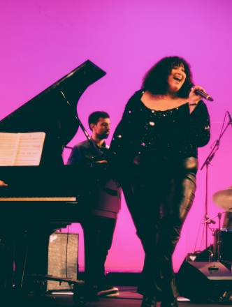 Woman singing with backup band in front of pink backgound