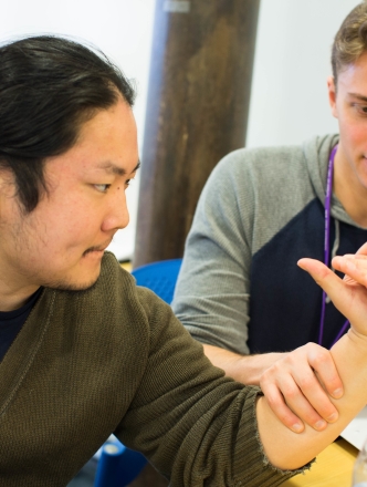 Two occupational therapy students do a wrist exercise together. 