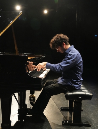 Piano student playing grand piano with spotlights on him