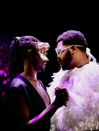 Two performers dressed with masks and a feathery costume doing a slow dance on stage