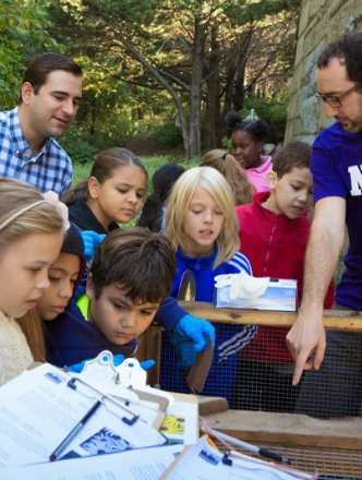 A man wearing an NYU shirt points into a tank as children peer inside.