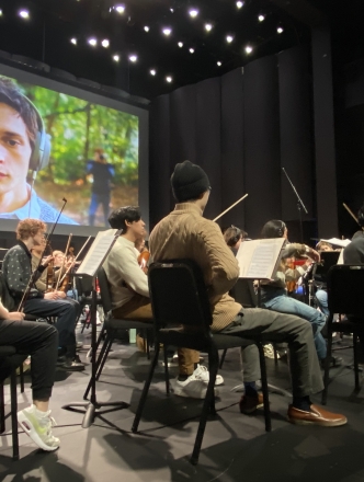 Students playing instruments in front of screen created by screen scoring students