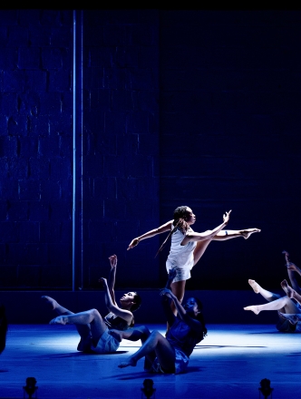 A central dancer in the spotlight with other dancers on the ground around her