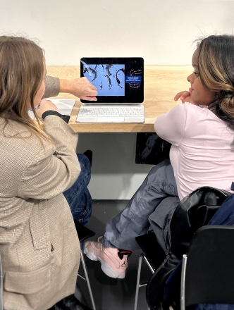 Two students sit in front of a laptop discussing the image on screen