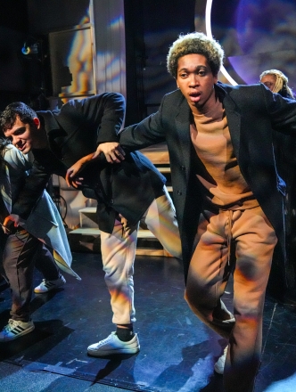 Group of actors hunched over walking toward camera on stage