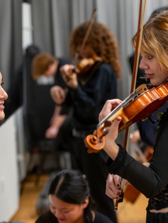 Two violinist collaborating while other students are in background
