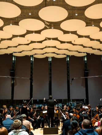 NYU Symphony perfoming in paulson center with massive lighting fixtures overhead