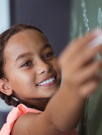 Young girl writing on chalk board.