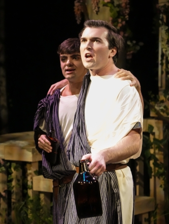 Two actors in costume on stage singing arm in arm