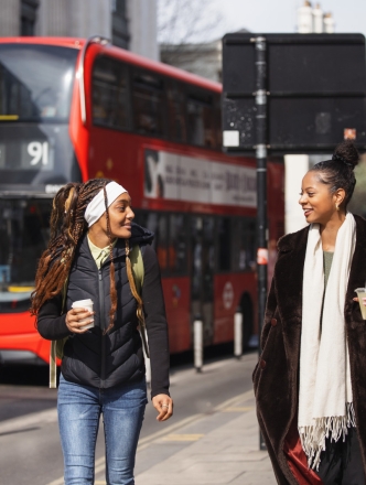 Two students walking in London with a red double decker bus behind them.