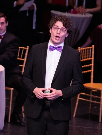 Opera singer on stage wearing a tuxedo and purple bow tie singing solo.