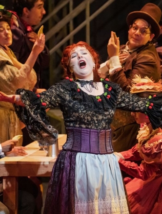 Woman singing lead on stage while backup singers sit and stand behind her,