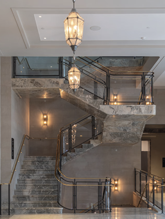 A stairway made of gray and white granite, thin gold hardware, and glass panels.