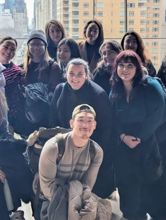 Large group of students standing in front of tall windows posing for the camera