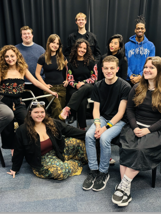 Group photo of the Village Voices ensemble posed around a piano