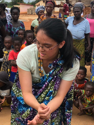 West African girl teaching student dance while group gathers to watch