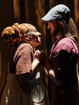 Two actors standing close holding hands and looking into each others eyes lovingly