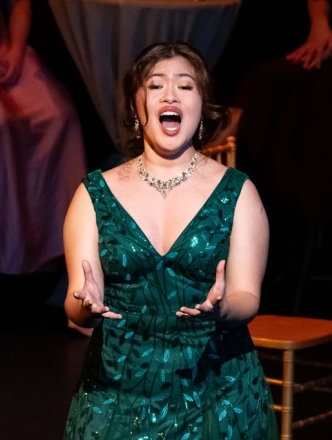 Student in V neck green sparkly dress singing opera on stage