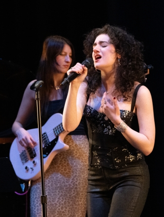 Student on stage singing into microphone with a guitarist backup