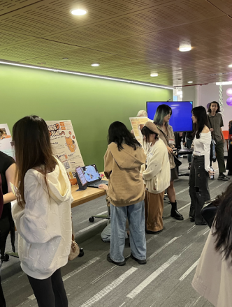 Students navigate around tables with boards and computers showcasing student work. 