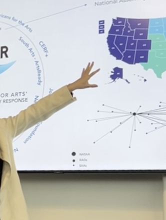 Presenter with long black hair discussing the arts across the US map