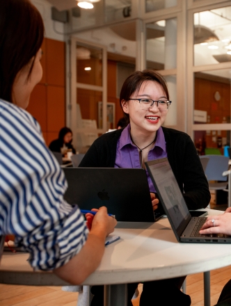 Three students talking around a small table. 