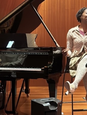 Woman sitting by piano singing into mic while student plays Steinway