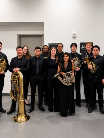 Brass Studies students posing for group photo before concert. Dressed in black and holding instruments.