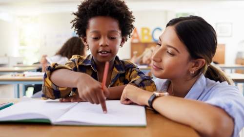 Teacher helping a student in a classroom setting.